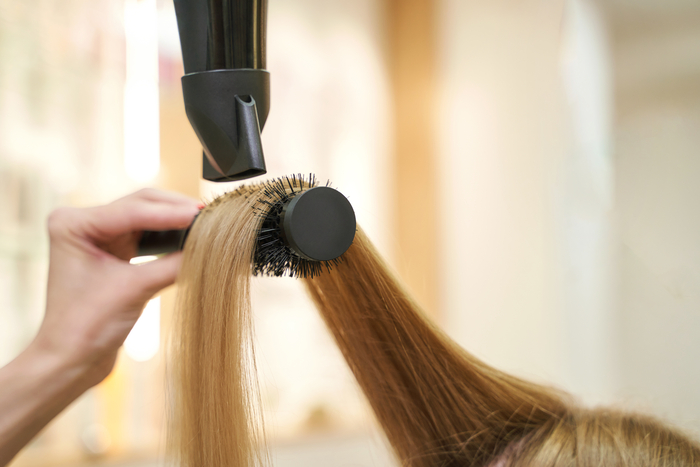Repair long hair procedure. Haircut at salon. Woman hairstyle. Master hand with brush and fan. Adult female person. Closeup view. Studio equipment. Lady preparation. Blonde dry. Copyspace