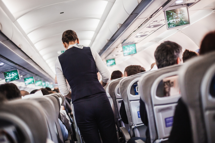 Interior of airplane with passengers on seats and stewardess in uniform walking the aisle, serving people. Commercial economy flight service concept.