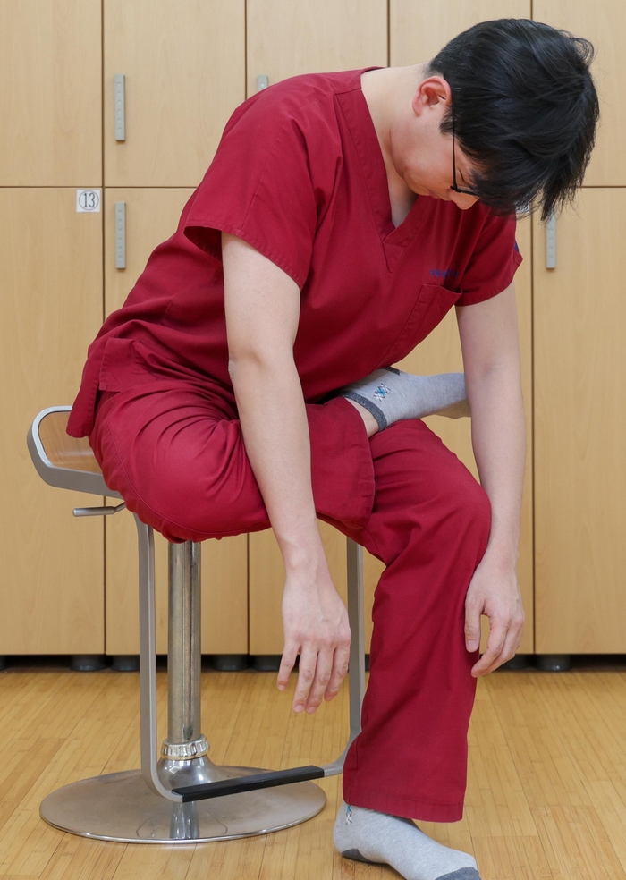의자에 앉아 한쪽 다리를 반대쪽 무릎 위에 올리고 상체를 천천히 숙이면 허리통증·요추긴장 완화에 효과적이다. 사진=경희대 한방병원